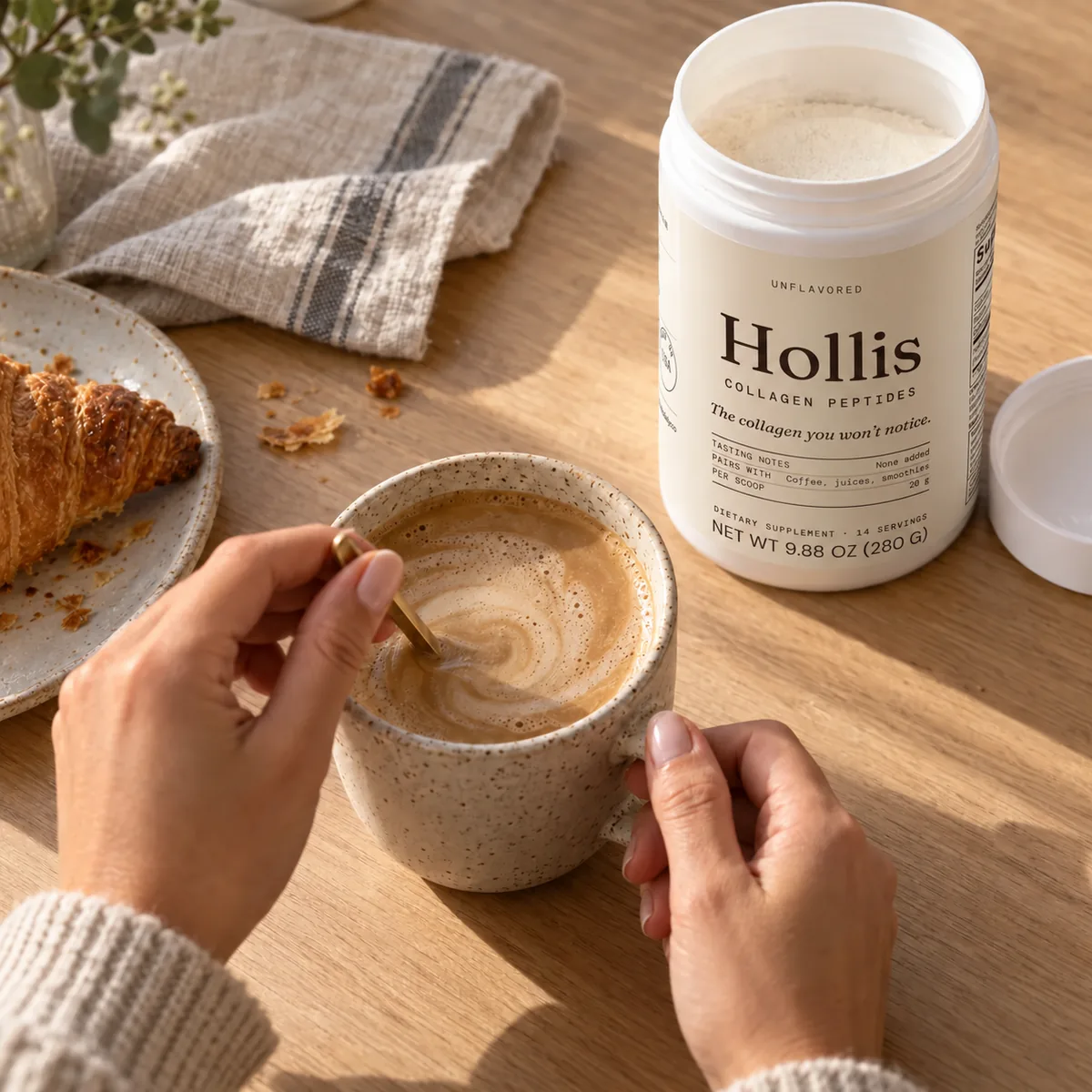 Hands stirring a mug of coffee beside the Hollis container